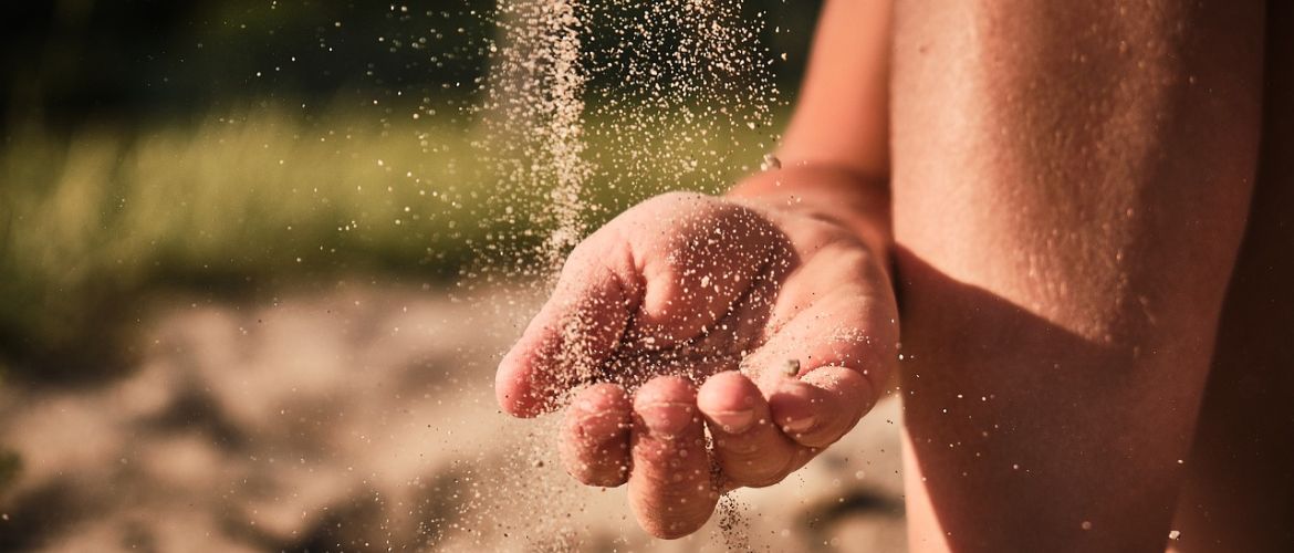 Sand rieselt auf eine Kinderhand